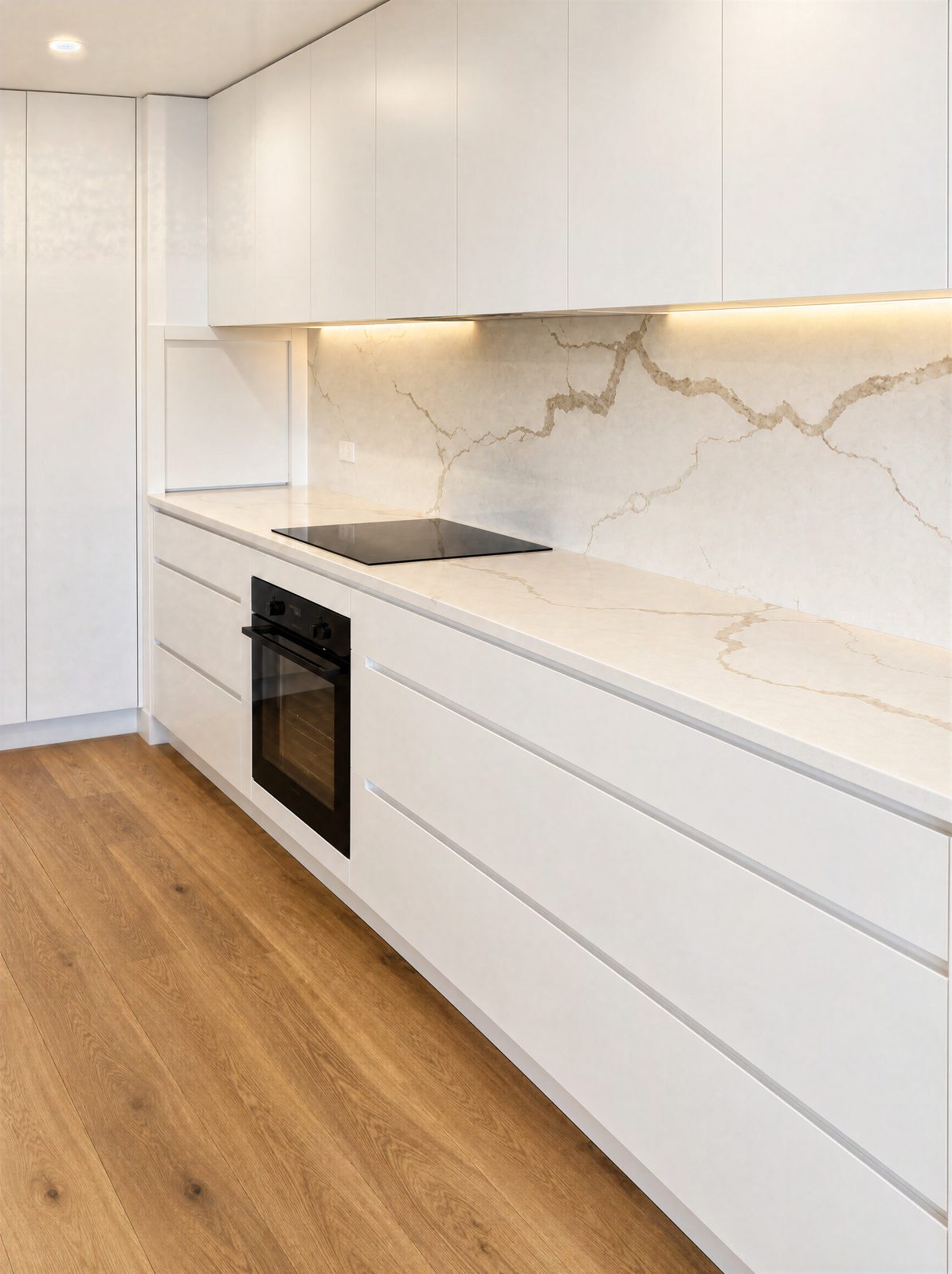 White handle-free kitchen with long drawers, a wall oven and overhead cabinets to the ceiling